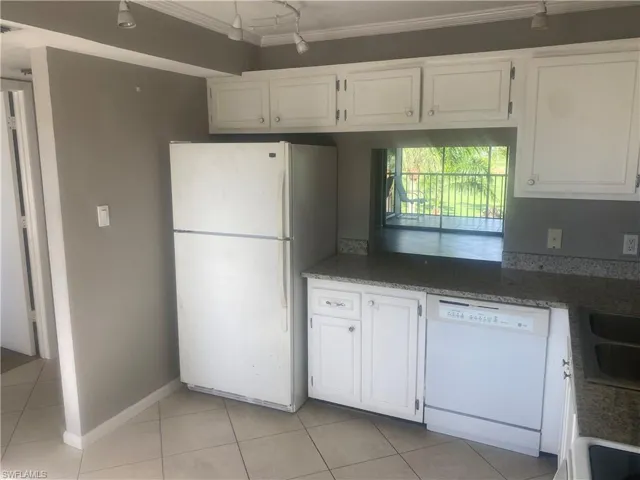 Kitchen with white appliances, white cabinetry, light tile patterned flooring, ornamental molding, and dark stone countertops