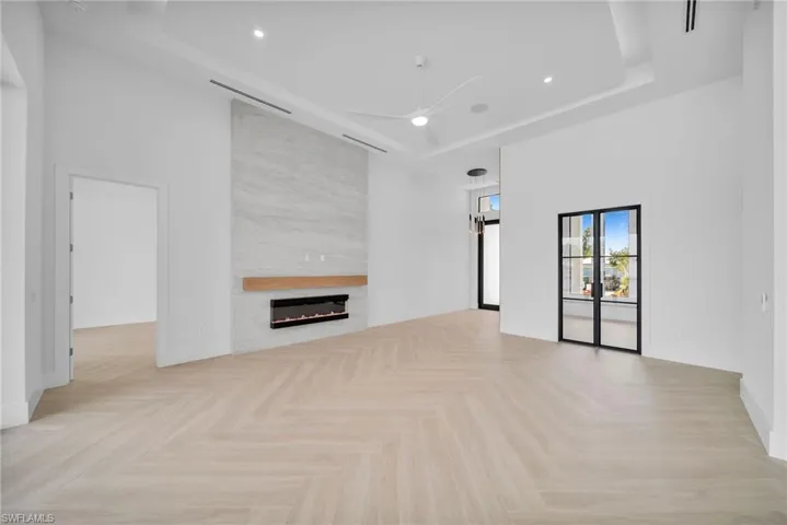 living room with a large fireplace, high ceilings, light flooring, and a tray ceiling