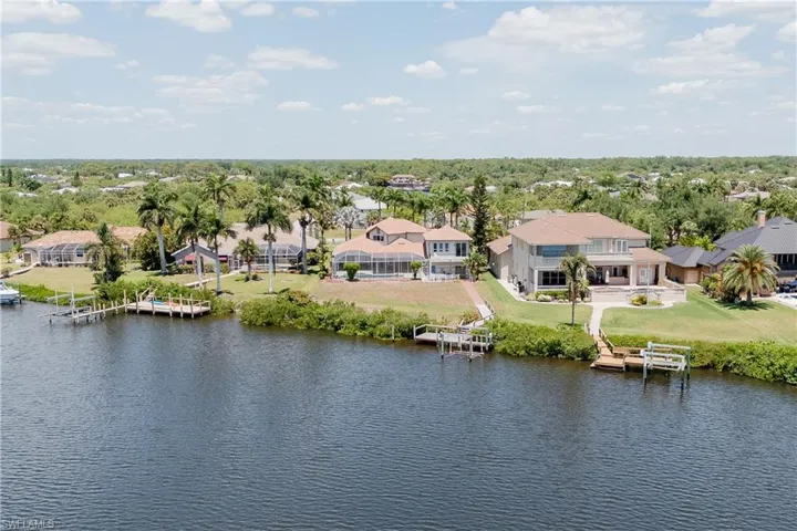 Waterfront property featuring multiple boat docks, mature palm trees, expansive rear patio