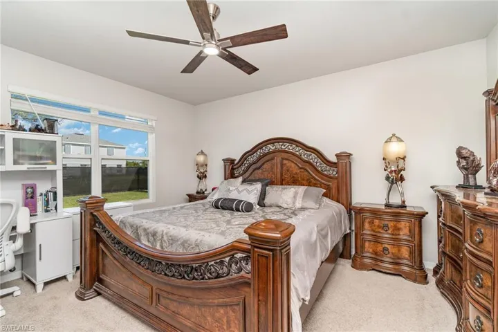 Bedroom featuring light carpet, a ceiling fan, and a desk