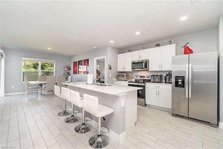 Kitchen featuring appliances with stainless steel finishes, a breakfast bar, a center island with sink, recessed lighting, and wood finish floors