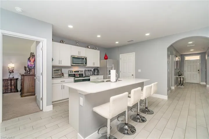 Kitchen featuring stainless steel appliances, light countertops, a kitchen bar, white cabinetry, and arched walkways