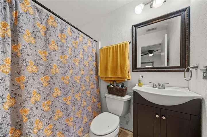 Full bathroom featuring a textured wall, a shower with shower curtain, vanity, and ceiling fan