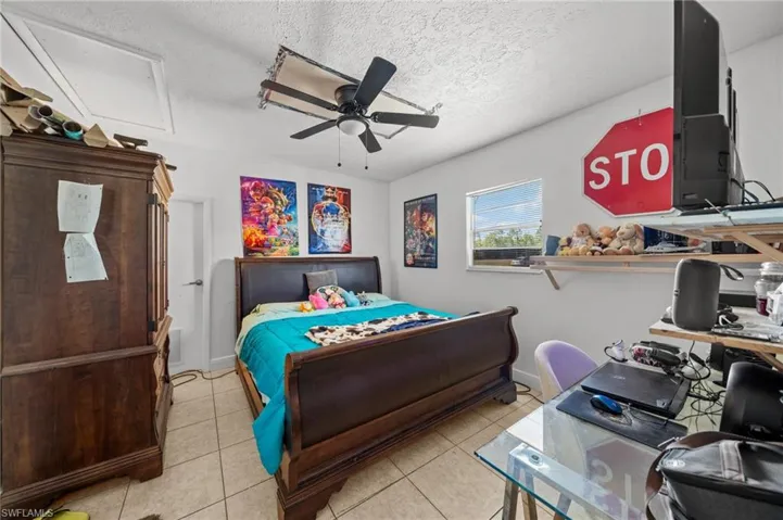 Bedroom with light tile patterned floors, a textured ceiling, a desk, a ceiling fan, and attic access