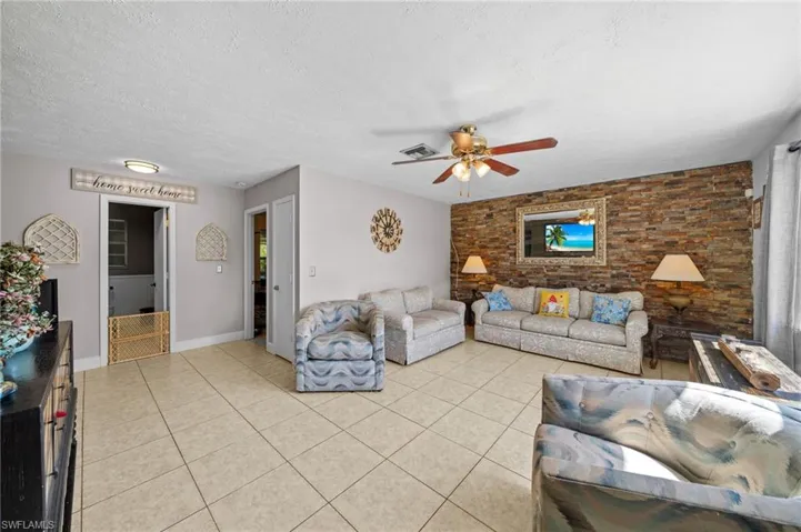 Living room featuring a textured ceiling, light tile patterned flooring, a ceiling fan, and an accent wall
