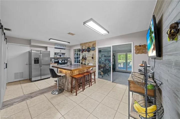 Kitchen featuring open shelves, a kitchen bar, stainless steel fridge, light tile patterned floors, and a barn door