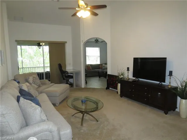 Living area with carpet, ceiling fan, arched walkways, and a high ceiling