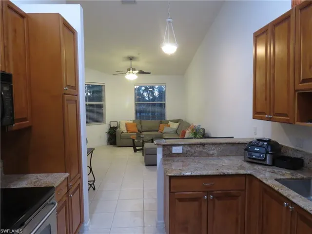 Kitchen with wood finish cabinets, stainless steel electric range, light stone counters, open floor plan, and lofted ceiling