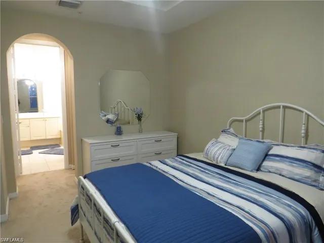 Bedroom featuring arched walkways, light colored carpet, and connected bathroom