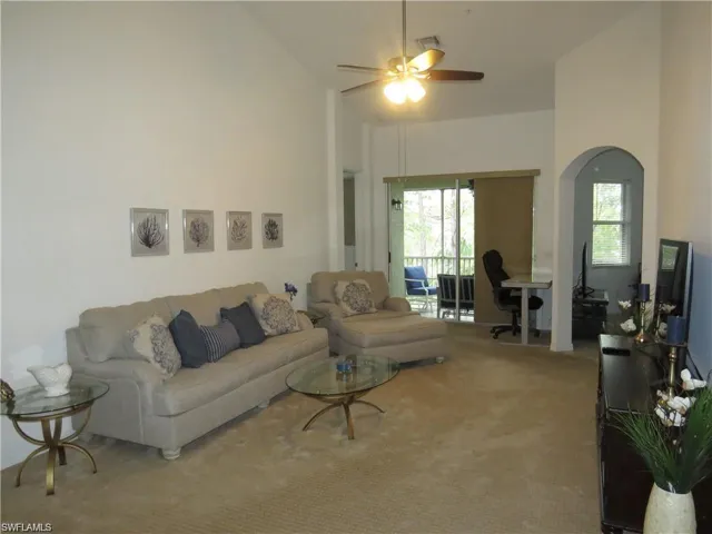 Carpeted living area featuring ceiling fan, vaulted ceiling, arched walkways, and an office area