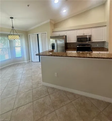 Kitchen featuring crown molding, lofted ceiling, stainless steel appliances, dark stone counters, and pendant lighting