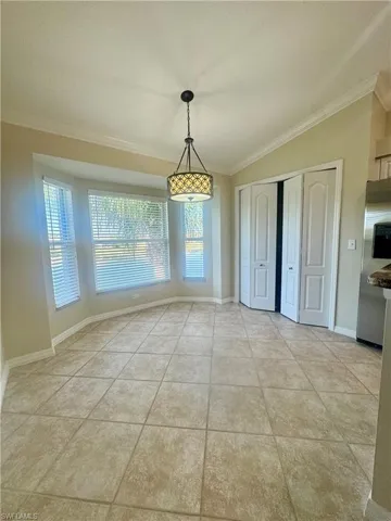 Unfurnished dining area with crown molding, vaulted ceiling, light tile patterned floors, and a textured ceiling