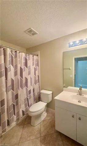 Full bath featuring vanity, a shower with shower curtain, a textured ceiling, and light tile patterned floors