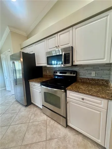 Kitchen featuring appliances with stainless steel finishes, white cabinets, ornamental molding, tasteful backsplash, and dark stone counters