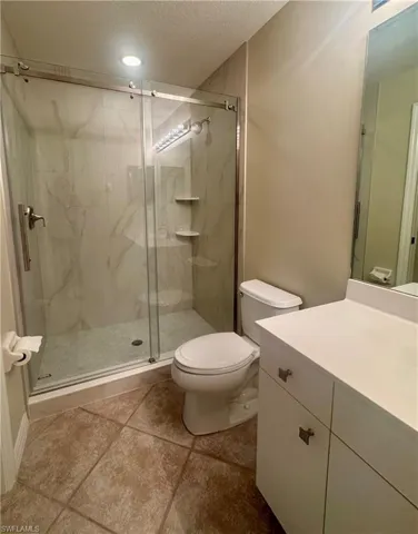 Full bathroom featuring a marble finish shower, a textured ceiling, vanity, and light tile patterned floors
