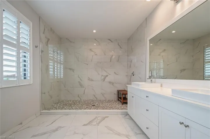 Bathroom with double vanity, a marble finish shower, and light marble finish floors