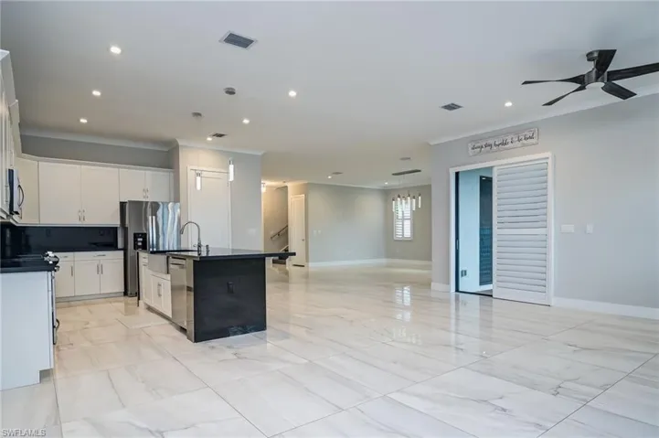 Kitchen with open floor plan, ornamental molding, an island with sink, light marble finish floors, and decorative light fixtures
