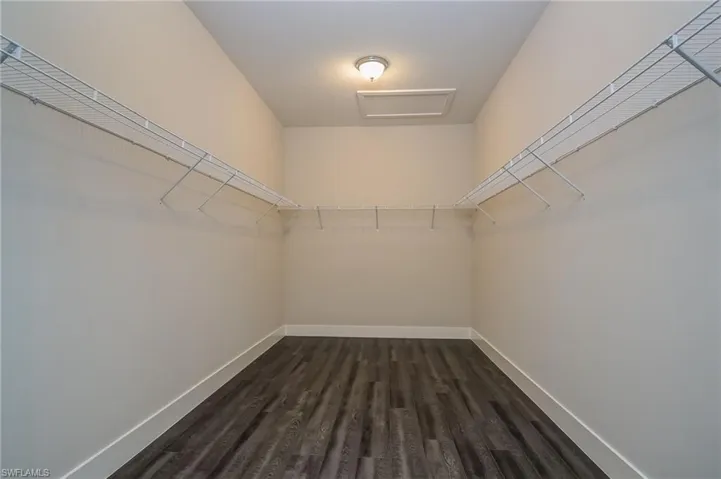 Walk in closet featuring attic access and dark wood-style floors