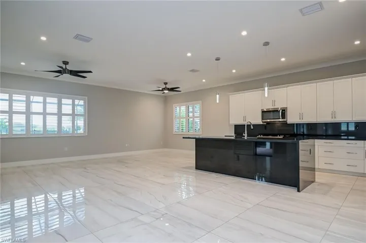 Dual tone kitchen featuring a kitchen island with sink, open floor plan, stainless steel microwave, pendant lighting, and ornamental molding