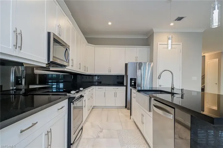 Kitchen with stainless steel appliances, tasteful backsplash, white cabinets, crown molding, and a center island with sink
