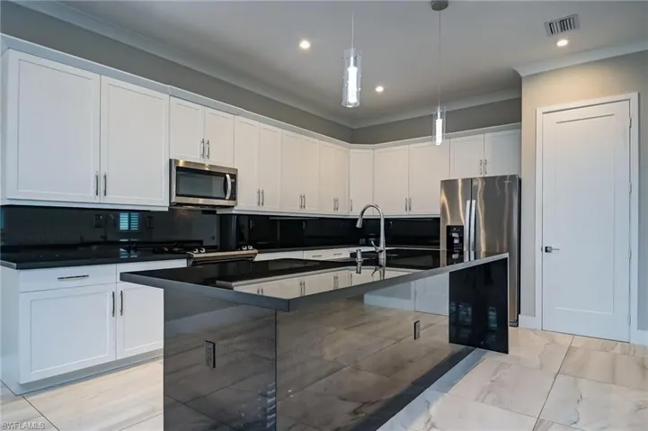 Kitchen with pendant lighting, a kitchen island with sink, stainless steel appliances, white cabinetry, and backsplash