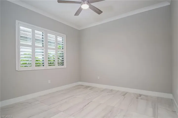 Unfurnished room featuring crown molding, a ceiling fan, and light marble finish floors