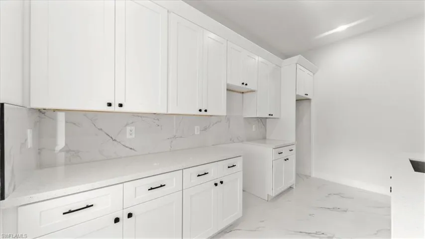 Kitchen with white cabinetry, light stone countertops, backsplash, and light marble finish flooring