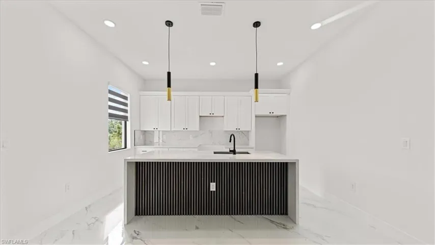 Kitchen featuring white cabinetry, light stone counters, recessed lighting, a kitchen island with sink, and light marble finish floors
