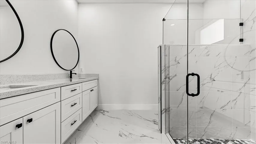 Bathroom with a marble finish shower, double vanity, and light marble finish floors