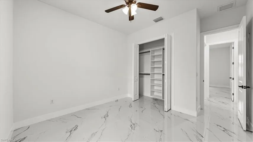 Unfurnished bedroom with light marble finish flooring, a closet, and a ceiling fan