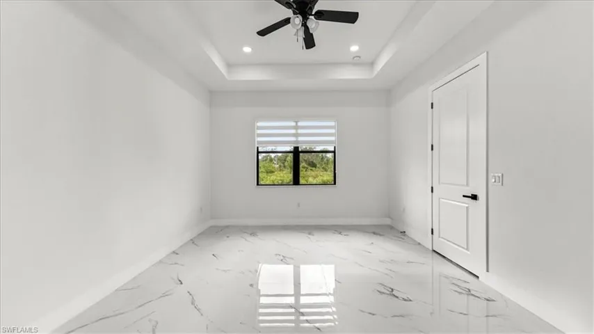 Empty room featuring light marble finish floors, recessed lighting, a tray ceiling, and a ceiling fan