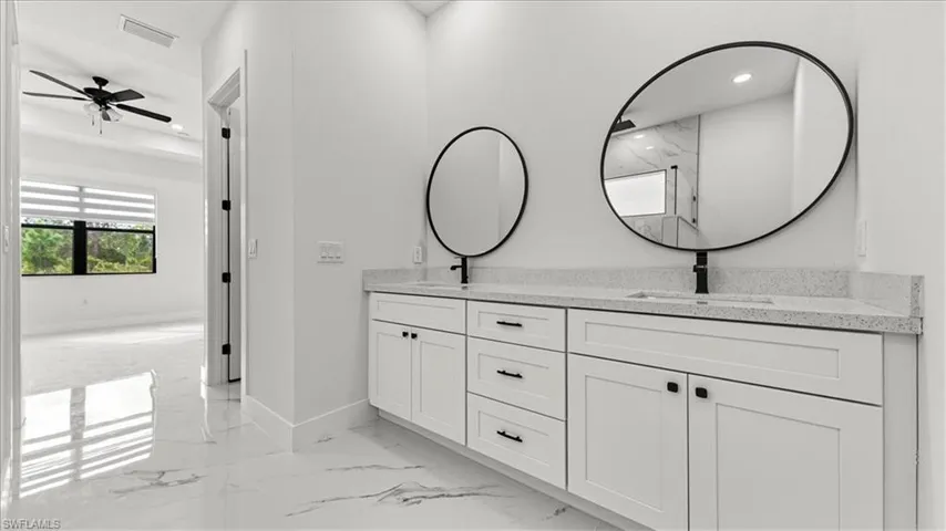 Bathroom with double vanity, light marble finish flooring, and recessed lighting