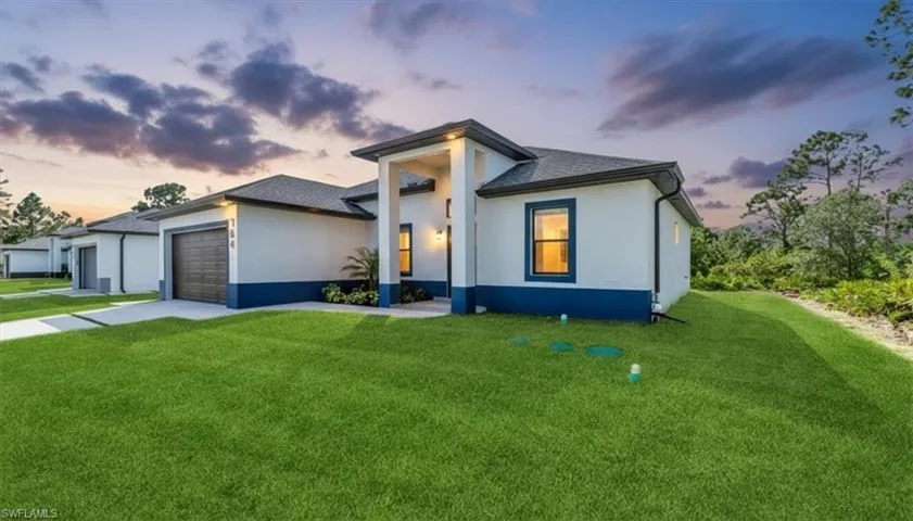 View of front of house with a yard, an attached garage, stucco siding, and driveway