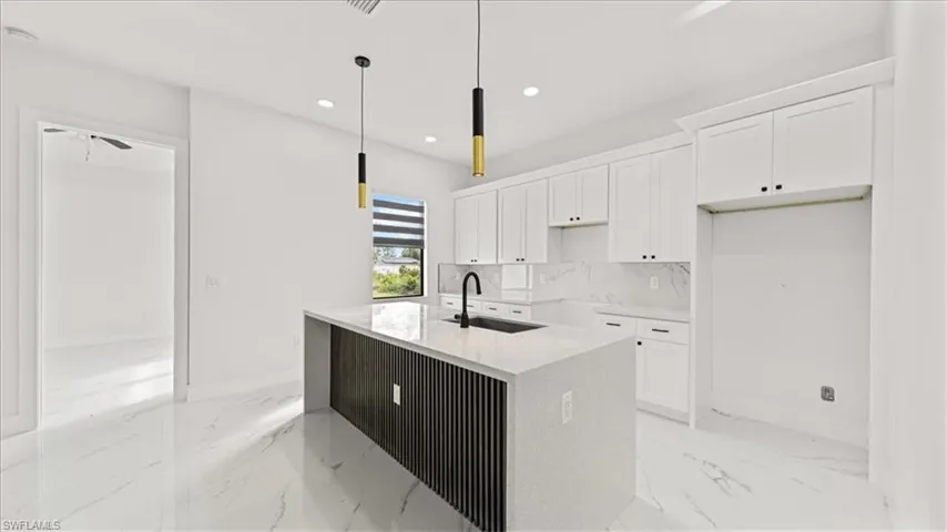 Kitchen featuring white cabinets, light stone countertops, backsplash, recessed lighting, and hanging light fixtures