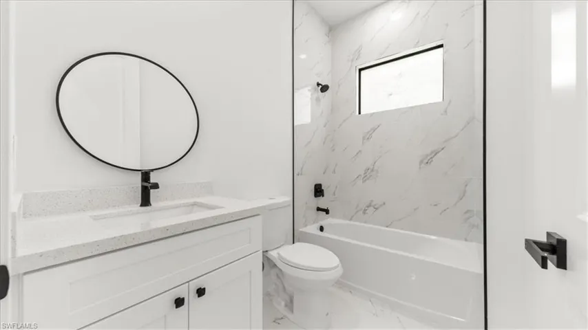 Full bath featuring vanity, washtub / shower combination, and marble finish floors