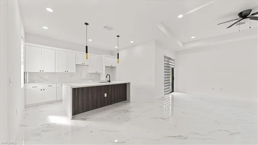 Kitchen with white cabinets, a kitchen island with sink, light stone countertops, recessed lighting, and light marble finish floors