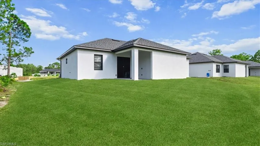 Back of property featuring a lawn, stucco siding, and a shingled roof