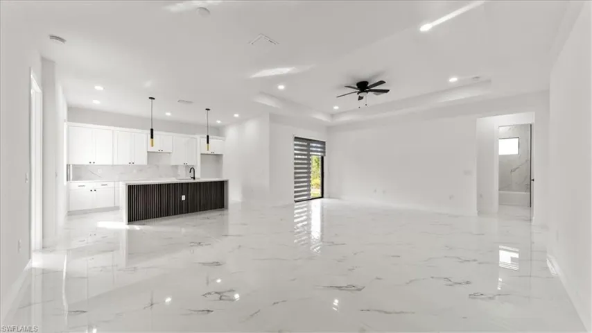Unfurnished living room featuring light marble finish flooring, recessed lighting, ceiling fan, and a tray ceiling