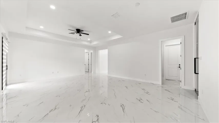 Unfurnished room with a raised ceiling, recessed lighting, light marble finish floors, and a ceiling fan