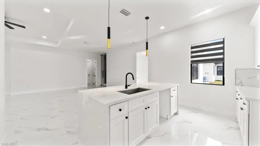 Kitchen featuring white cabinets, decorative light fixtures, recessed lighting, light stone counters, and light marble finish floors