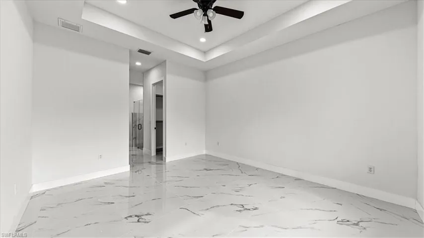 Empty room with a tray ceiling, light marble finish floors, recessed lighting, and a ceiling fan