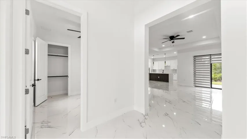 Hall featuring recessed lighting, light marble finish floors, and a tray ceiling