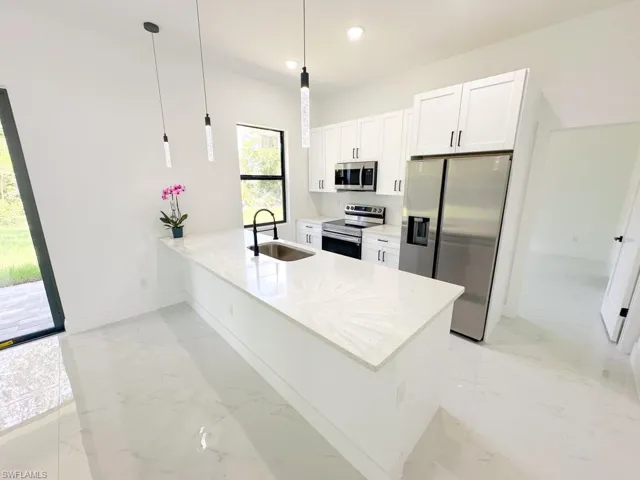 Kitchen with white cabinetry, stainless steel appliances, pendant lighting, sink, and light tile flooring