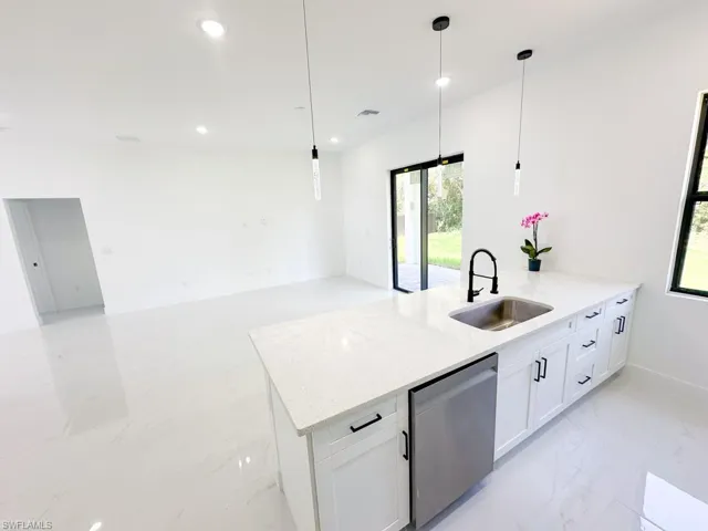 Kitchen featuring white cabinetry, light stone countertops, sink, light tile floors, and pendant lighting