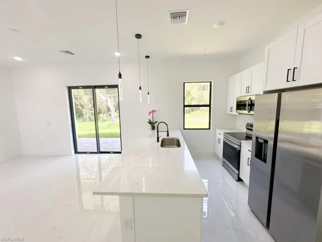 Kitchen with stainless steel appliances, an island with sink, pendant lighting, sink, and light tile flooring