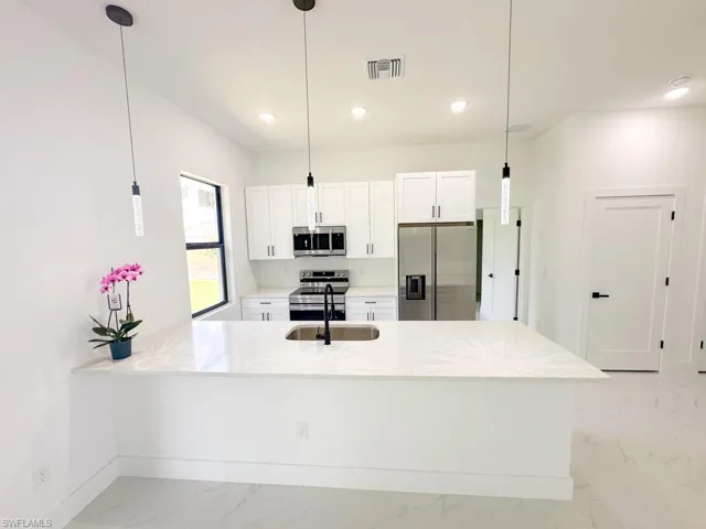 Kitchen with stainless steel appliances, white cabinets, and pendant lighting