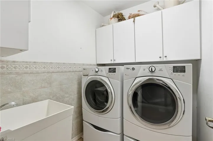 Laundry room with washer and dryer, tile walls, cabinet space, and wainscoting - Virtually Edited Image
