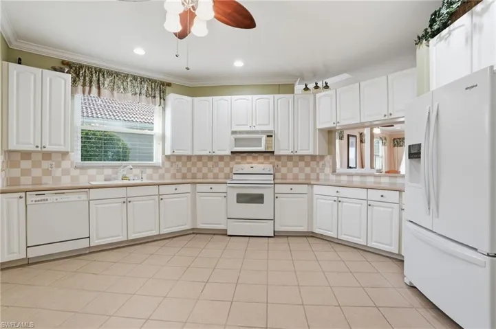 Kitchen featuring white appliances, white cabinetry, a ceiling fan, crown molding, and recessed lighting - Virtually Edited Image