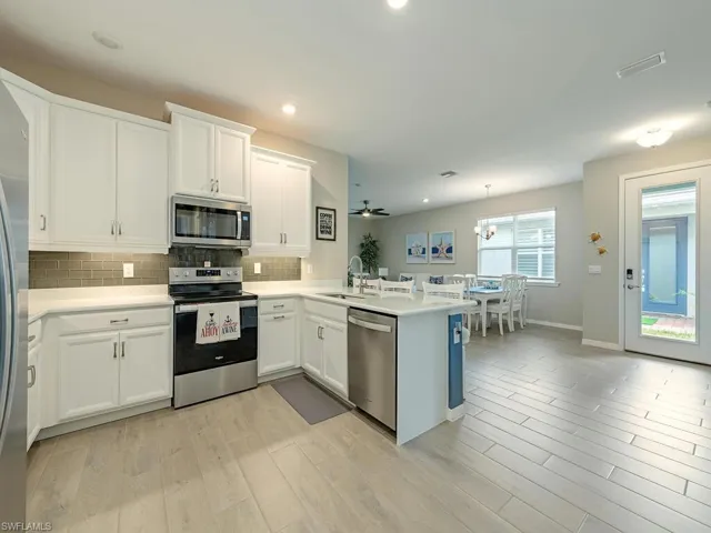 Kitchen with appliances with stainless steel finishes, light hardwood / wood-style flooring, sink, kitchen peninsula, and white cabinetry