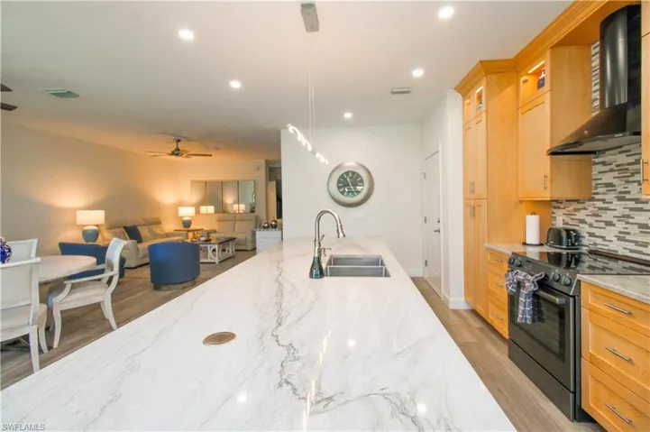 Kitchen featuring tasteful backsplash, black electric range oven, light stone counters, wall chimney range hood, and sink